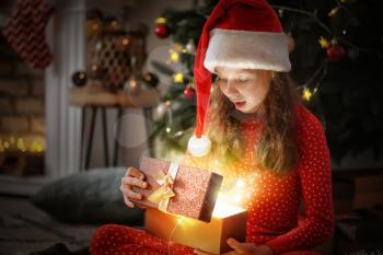 Cute little girl opening magic Christmas gift at home�