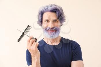 Mature male barber with dyed hair and beard on light background�