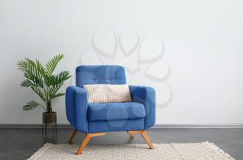 Comfortable blue armchair and houseplant near light wall�
