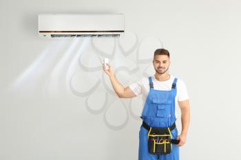 Male technician switching on air conditioner on light wall�