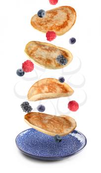 Tasty pancakes and berries falling on plate against white background�