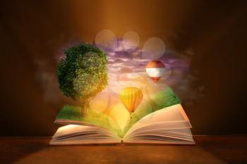 Open magic book with flying hot air balloons and growing tree on dark background�