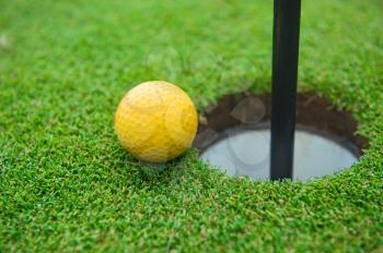 Golf ball on the edge of hole on the green grass