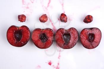 image of fresh cherries cut in halves with seeds  and cherry juice on white