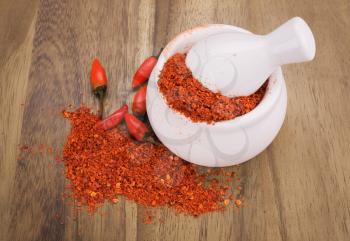 Crushed red hot chili peppers in a bowl over wooden background