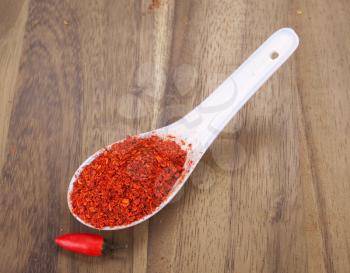 Crushed red hot chili peppers in a spoon over wooden background