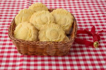 Some decorated traditional  butter biscuits in the wicker basket and christmas bell on checkered tablecloth