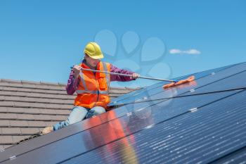 young worker cleaning solar panels on house roof