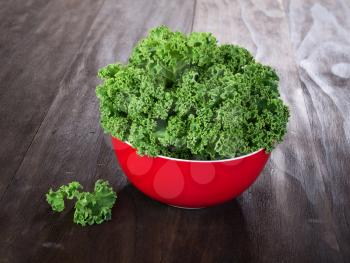 fresh green kale leaves in red ceramic bowl on vintage wooden table