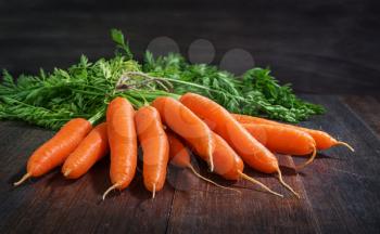 Bunch of fresh carrots vegetables with green leaves on rustic wooden background