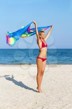 Dreamy lovely teen girl standing on the beach with pareo in hands