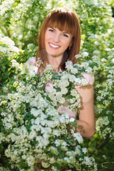Pretty red-haired smiling woman posing near the flowering bush