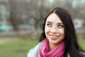 Portrait of pretty smiling brunette with pink scarf posing outside
