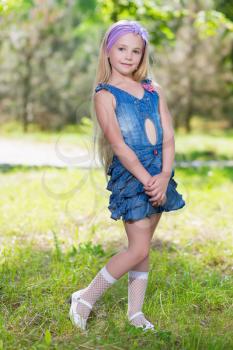 Little blond girl posing in jeans dress outdoors