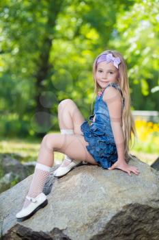 Pretty little girl in jeans dress sitting on the stone