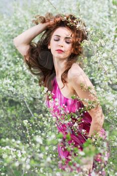 Curly brunette playing with her hair and posing in flowering trees