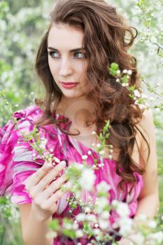Pretty curly lady wearing pink dress touching the branch of flowering tree