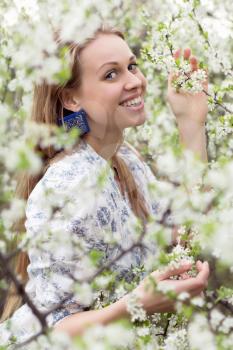 Portrait of young smiling blonde touching the branch of flowering tree