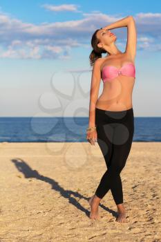 Slim young woman in black leggings and pink bra on the beach
