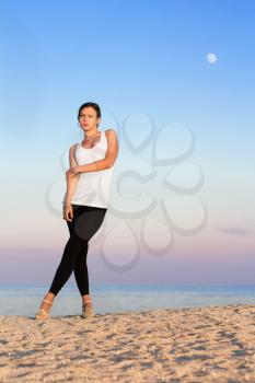 Pretty woman in white t-shirt and tight black leggings posing on the beach
