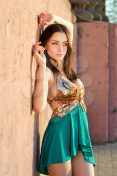 Attractive young lady in golden and turquoise dress posing near the wall outdoors