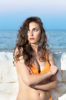 Curly thoughtful lady posing near a stone fence on the beach