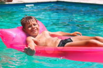 Smiling boy lies on pink mattress in the pool