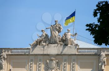 The upper part of Ivan Franko National University main building with National Flag of Ukraine.  Allegorical sculpture composition Galicia, Vistula and Dniester. Lviv, Ukraine