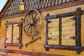 Old style wooden cottage with decorative wheel between shuttered windows