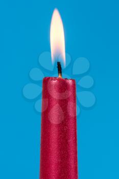 Burning red candle over a blue background