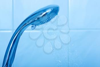 Shower head with water stream on blue background 