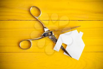 Scissors and house cut out of paper on the yellow background