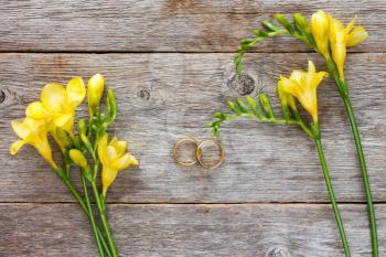 Wedding rings and freesia flowers on wooden background. Top view.