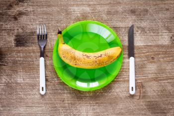   Fork,knife and green plate with banana on wooden background.