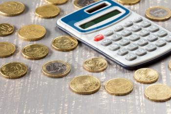  Euro coins and digital calculator on wooden background