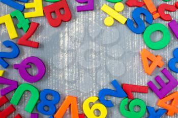 Border of colorful toy magnetic letters and numbers over a  grey wooden background