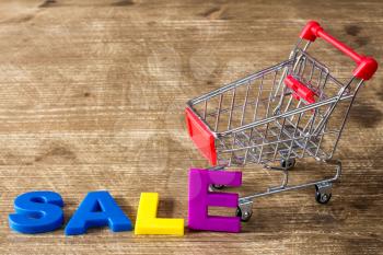  Shopping cart and color letters spelling SALE on wooden background