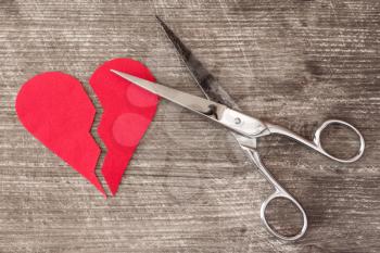 Broken red heart and scissors on a wooden background