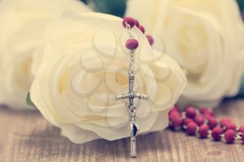 Catholic rosary and white roses on wooden background. Religion concept.