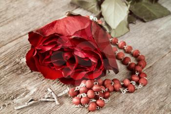 Catholic rosary and red rose on old wooden background