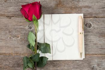 Old rose and blank paper sheets with pen on wooden background