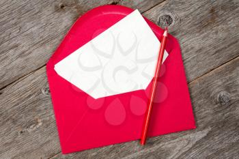 Blank paper, red envelope and pencil on wooden background