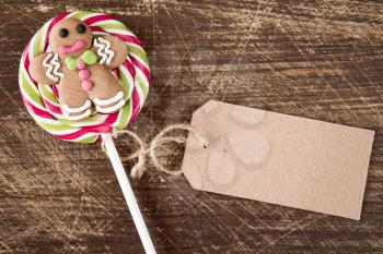 Christmas lollipop with gingerbread man and blank price tag on wooden background