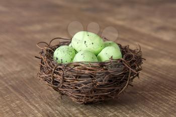 Decorative green eggs in nest on wooden background