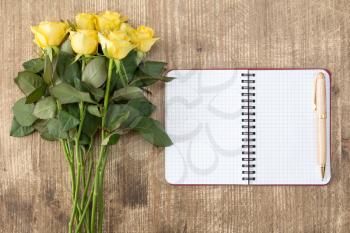 Blank notebook and bunch of yellow roses on the wooden table