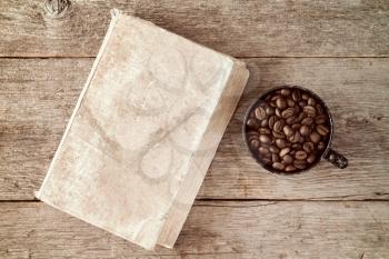Black coffee cup and coffee beans with old book on wooden background 