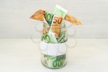 Euro bills in glass jar on wooden background. Saving money concept