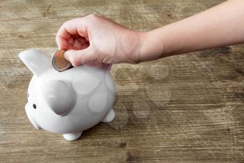 Child's hand putting a coin into piggy bank