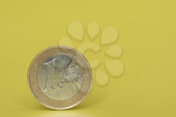 One euro coin stands on yellow background
