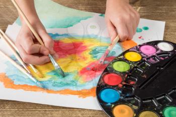 Child painting with paintbrush and colorful paints